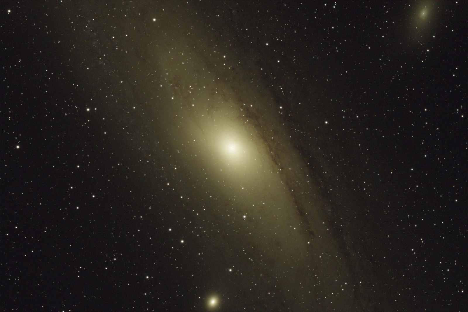 The Andromeda galaxy filling the frame at a tilt, a bright core, dark dust lanes across the far arm, the small companion galaxy M32 below it and the fainter M110 in the upper corner, against a field of foreground stars.